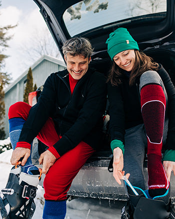 people sitting on a car putting on their ski and snowboard boots wearing usa new hampshire made mountain heritage elite socks