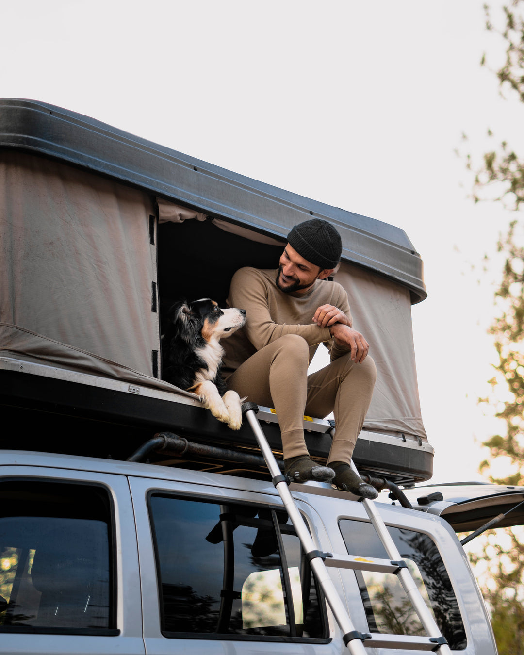 A man sits at the opening of a pop-up camper staring at his dog