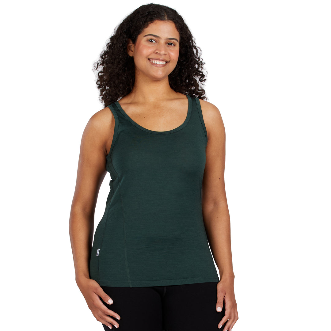 A woman with curly dark hair wearing a dark green 100% Merino Wool athletic tank top and black leggings, standing against a solid white background. 