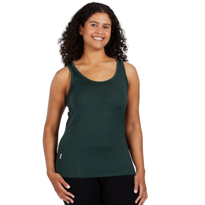 A woman with curly dark hair wearing a dark green 100% Merino Wool athletic tank top and black leggings, standing against a solid white background. 