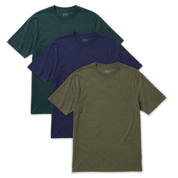 Three short-sleeve merino crewneck t-shirts in green, navy blue, and olive drab, arranged in a cascading stack on a white background. Merino t shirt for men