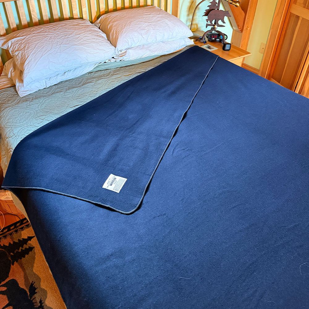 king sized wool blanket blue merino, draped over a bed in a bedroom setting 