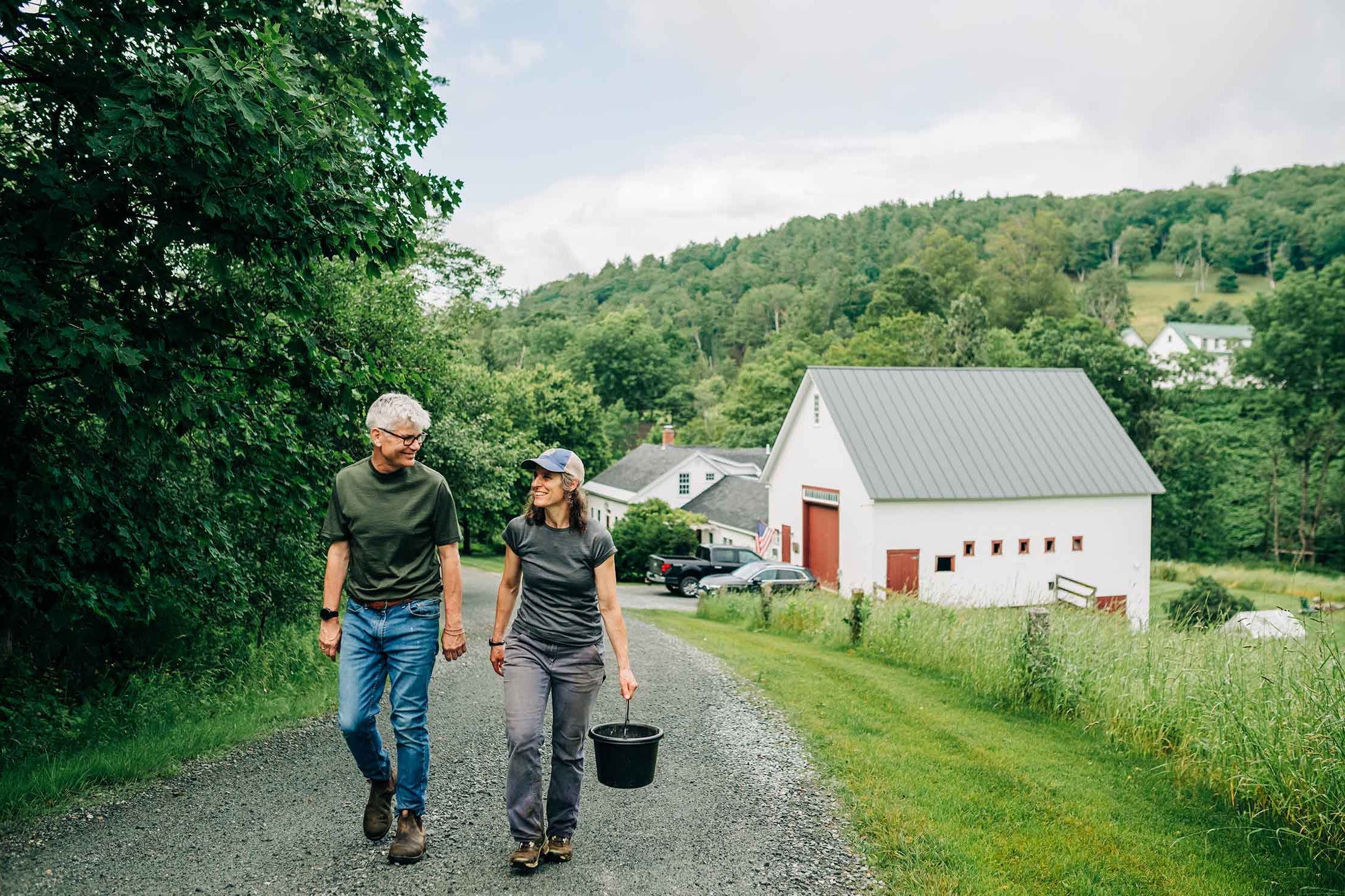 Two people walking on a path with a white barn and green hills in the background  wearing minus33 lightweight merino wool 