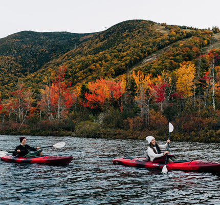 Photo of Man and woman kayaking on a pond surrounded by fall foliage wearing Merino wool 