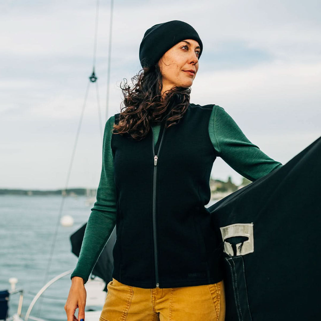 Woman wearing a green and black merino wool sweater vest jacket with a sailboat in the background #color_black